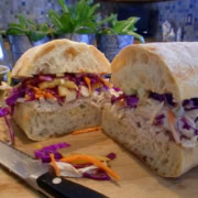 A chicken sandwich with cole slaw on a cutting board.