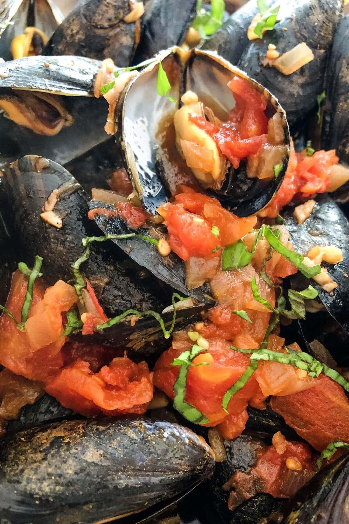 Cooked mussels with marinara sauce and fresh basil.