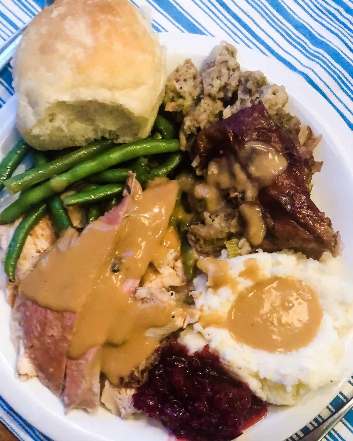 plate of mashed potatoes, grilled turkey, cranberry sauce, green beans and dinner roll