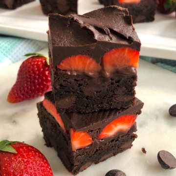 Two brownies with fresh strawberries topped with chocolate.