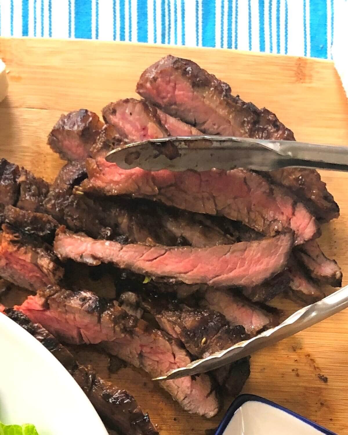 Slices of skirt steak and tongs.