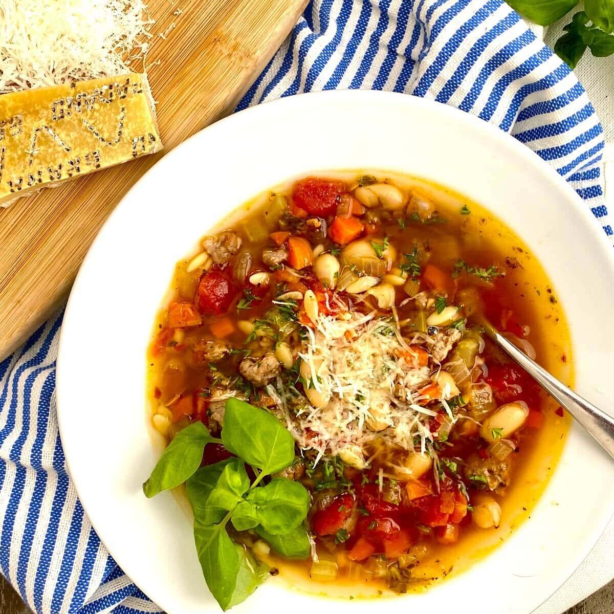 A bowl of pasta e fagioli with sausage with fresh basil.