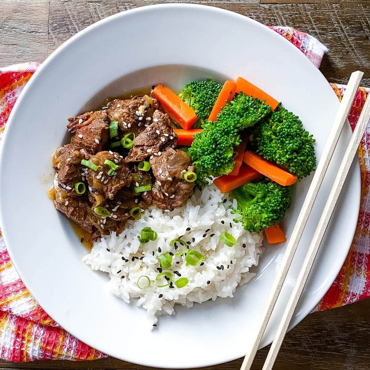 A bowl of Instant Pot Asian beef stew with rice, vegetables and chopsticks.