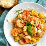 A bowl of shrimp with goat cheese over shell pasta.