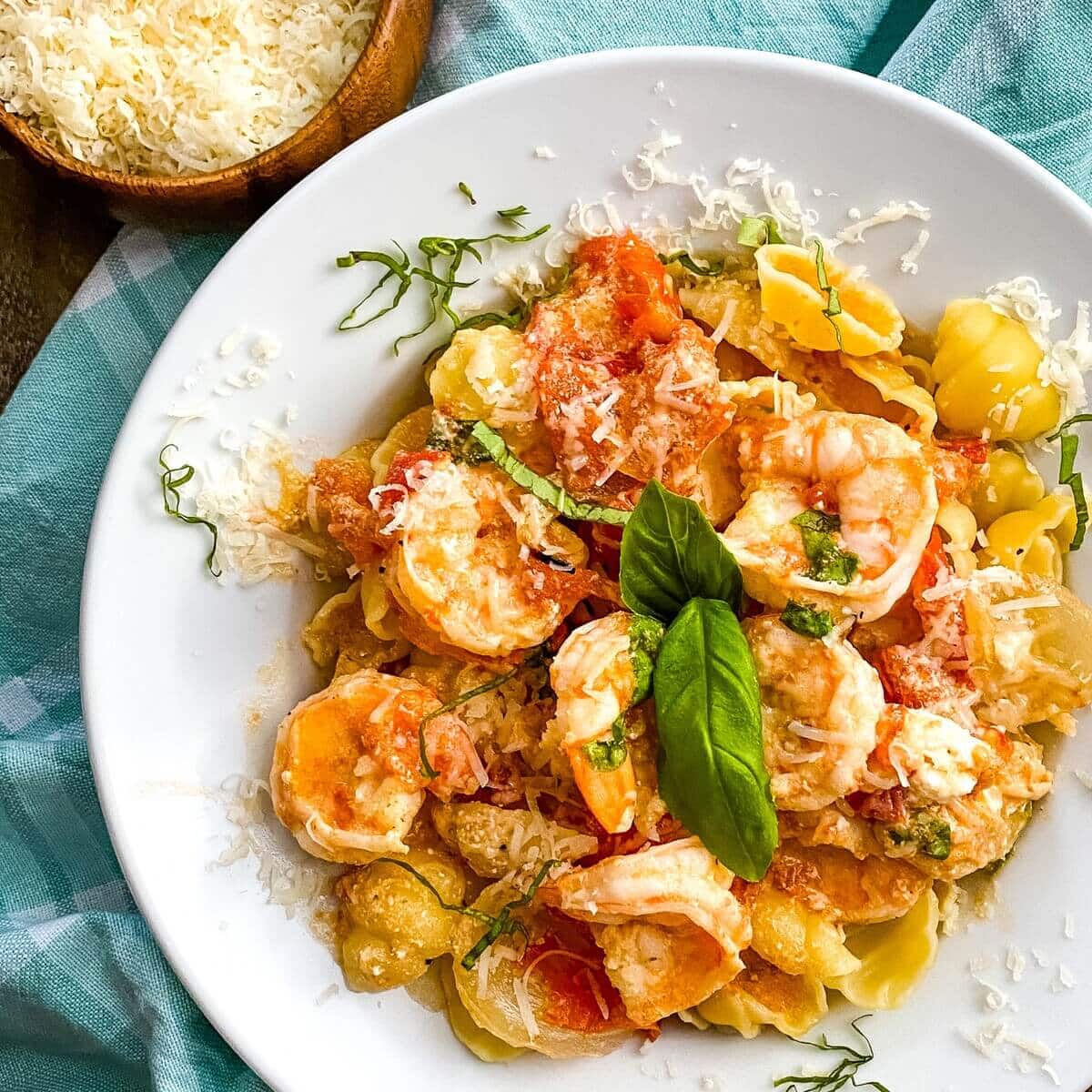 A bowl of shrimp with goat cheese over shell pasta.