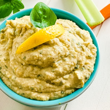 bowl of basil hummus with celery and carrot sticks