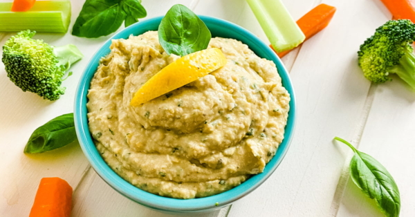 bowl of basil hummus with celery and carrot sticks