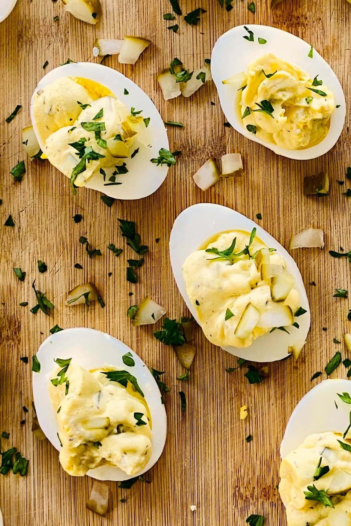 4 deviled eggs with dill pickles on a cutting board.