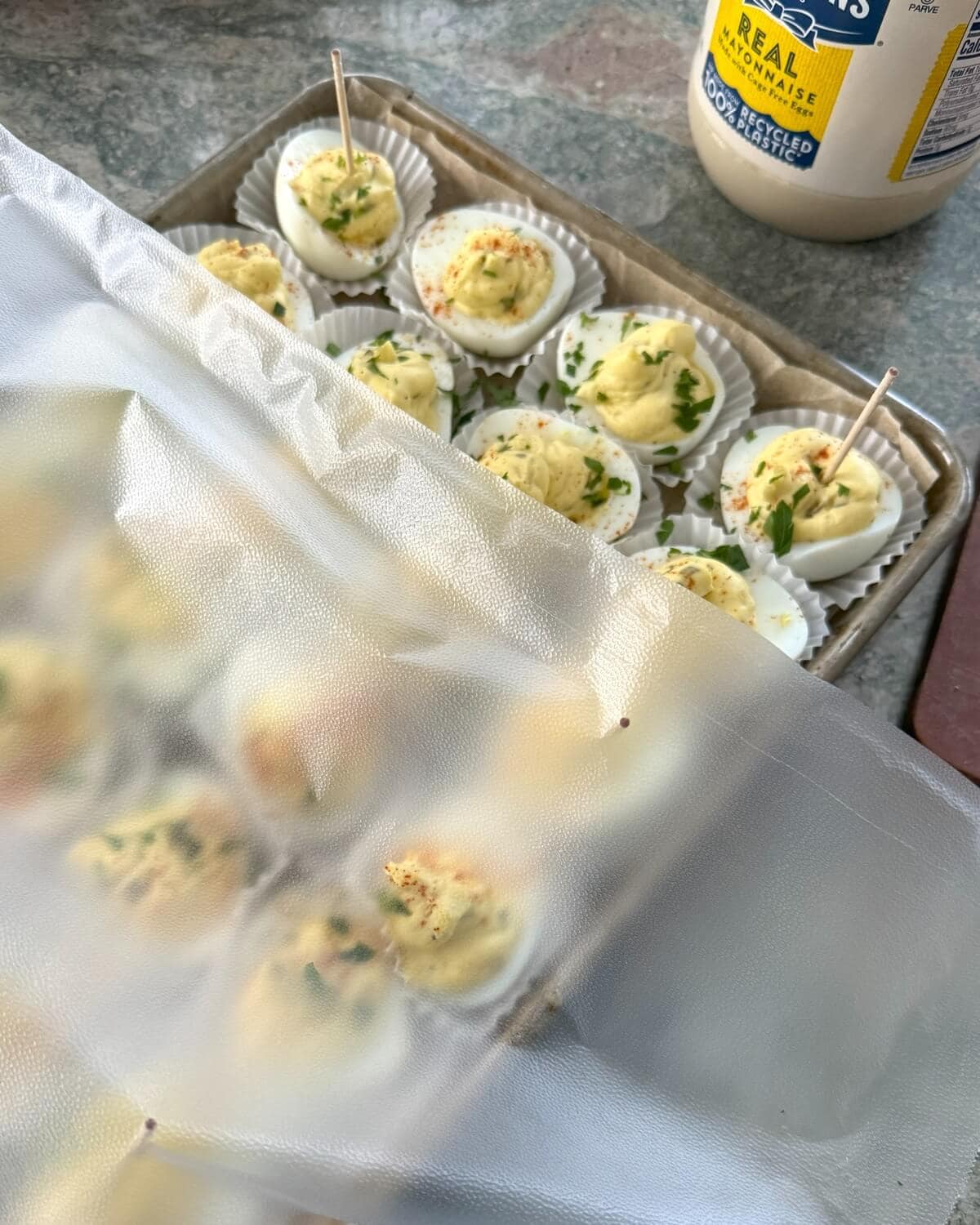 Stuffed eggs on a sheet pan with plastic wrap.