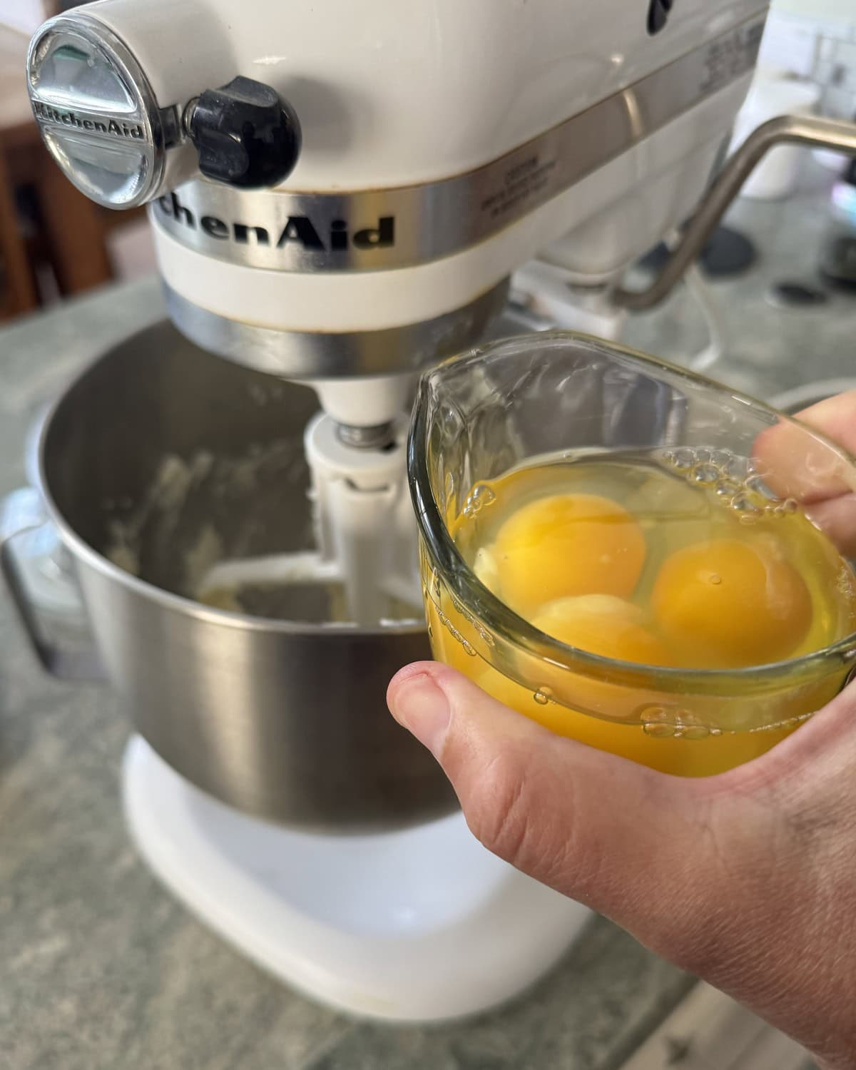 Adding eggs to a mixing bowl of a stand mixer.