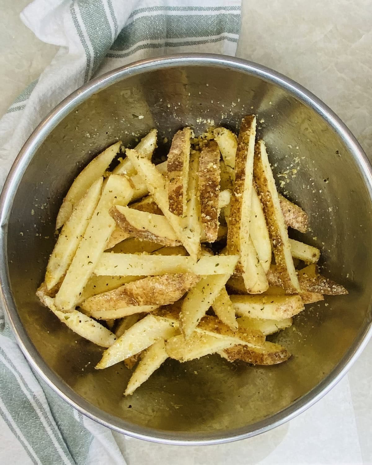 A bowl of cut potatoes and seasoned.