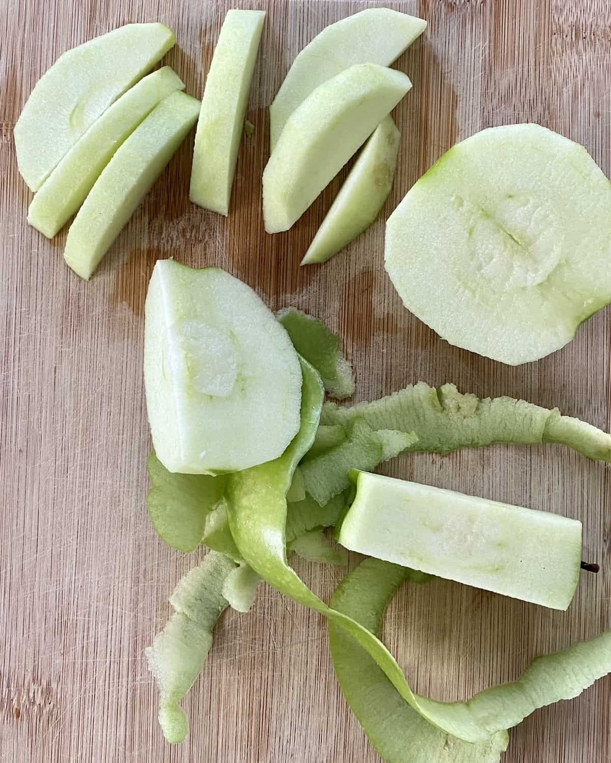 A peeled and sliced Granny Smith apple on a cutting board.