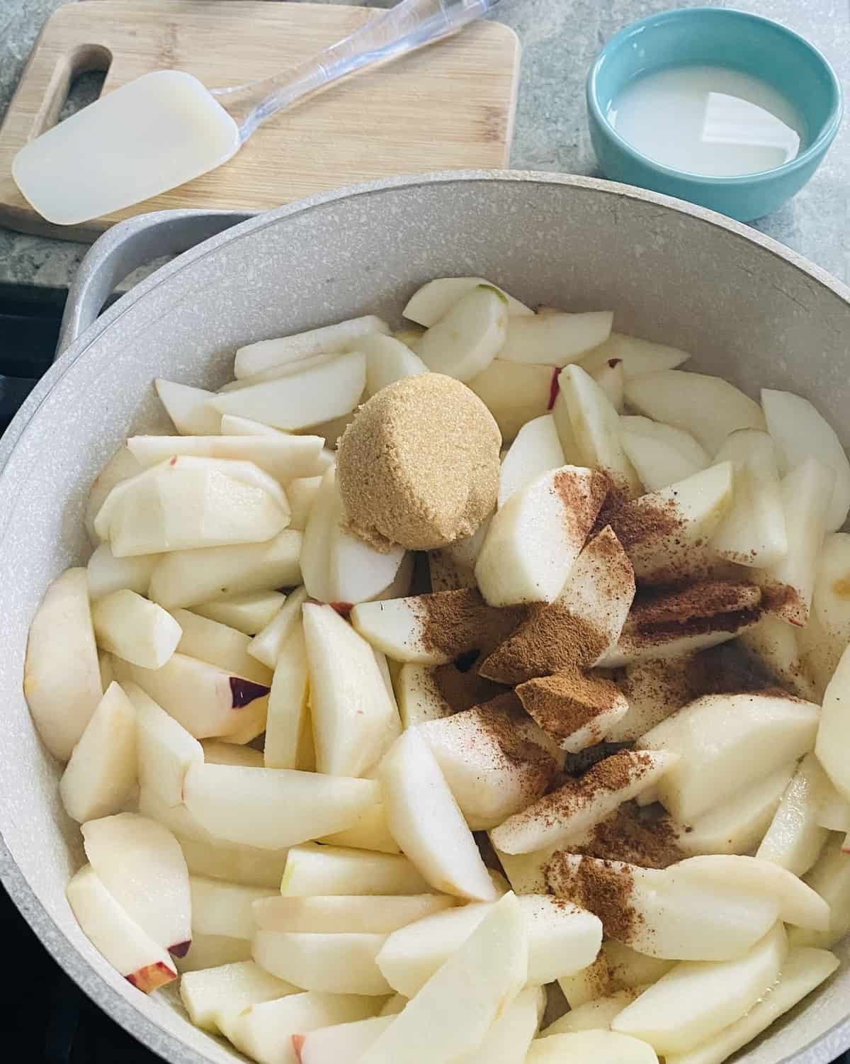 Uncooked peeled apple slices, cinnamon and brown sugar in a sauté pan.