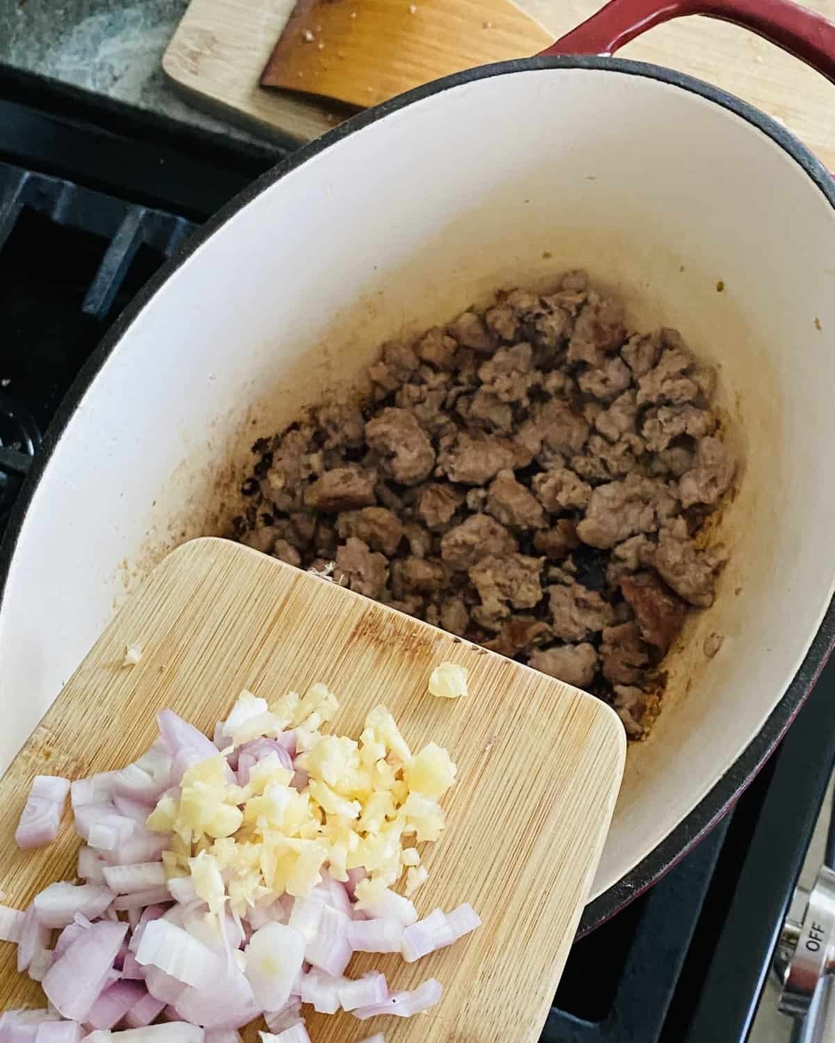 adding chopped shallot and garlic to cooked Italian sausage.