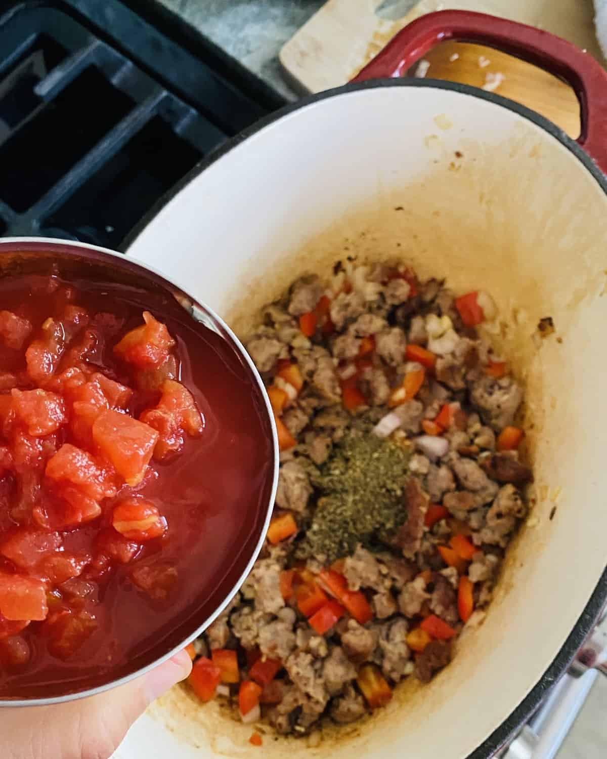 adding canned tomatoes to cooked Italian sausage