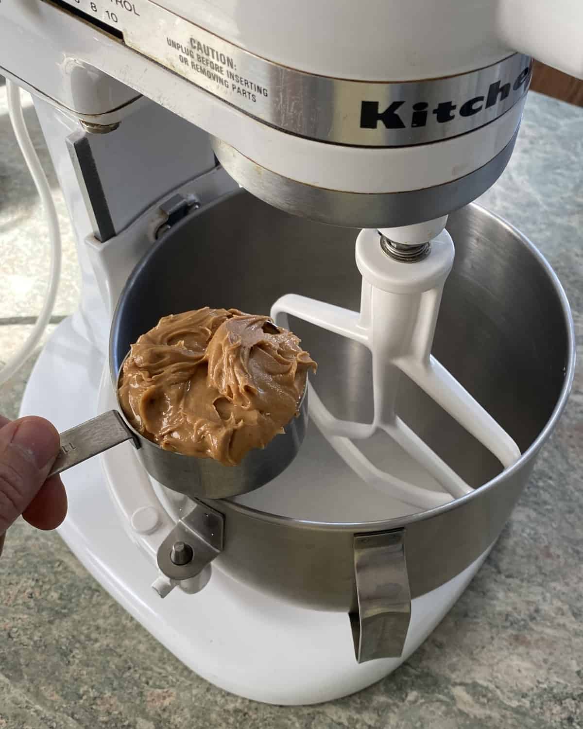 adding peanut butter to bowl of stand mixer