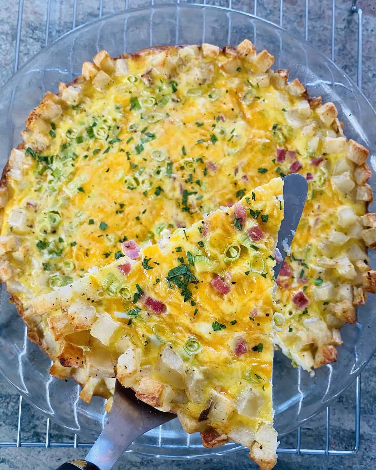 A slice of hash brown crust quiche with ham and cheddar cheese.