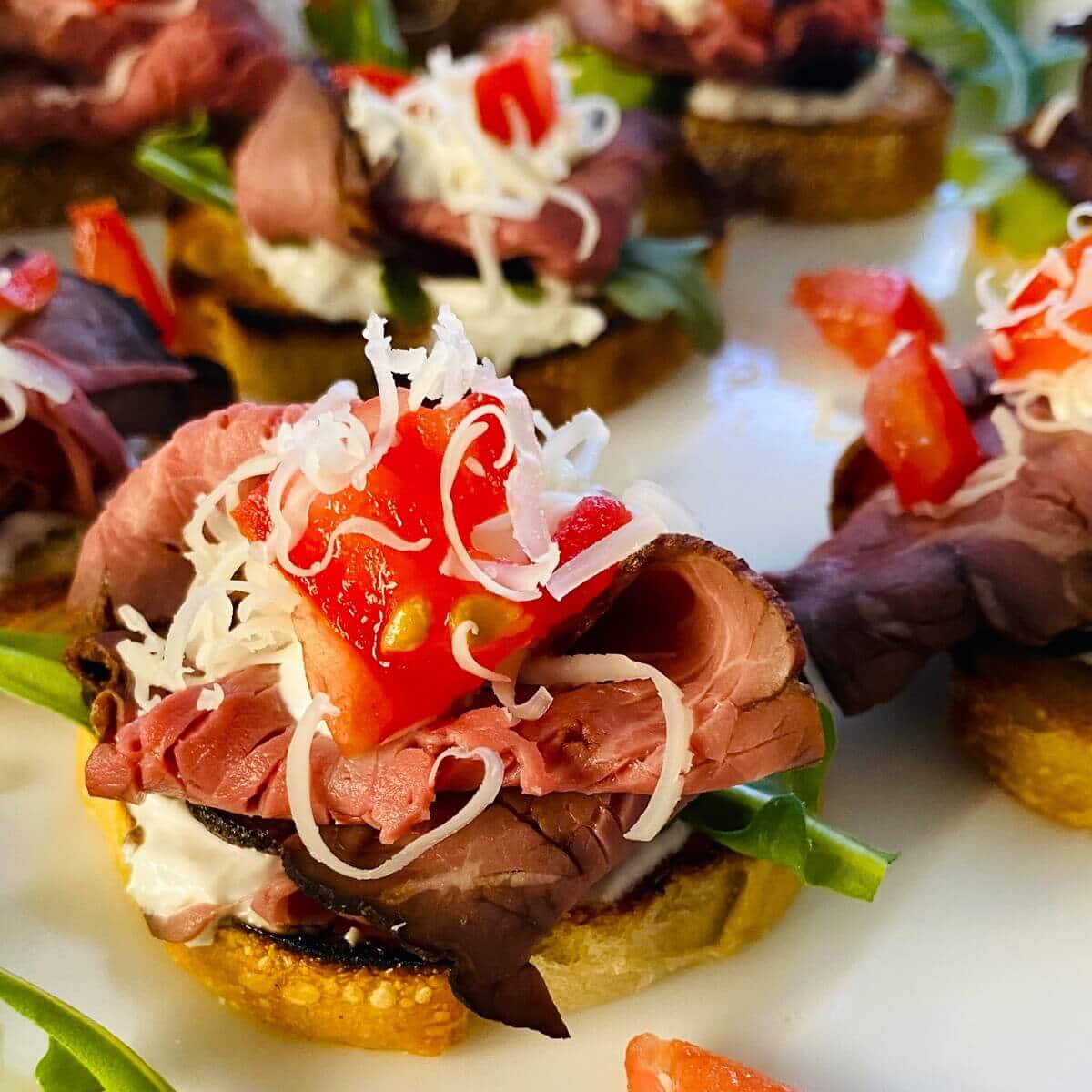 Crostini topped with roast beef, horseradish cream, arugula, and tomatoes.