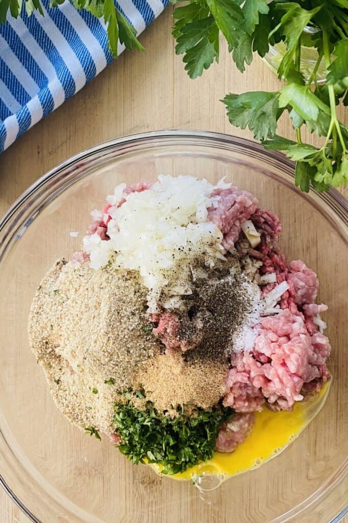 ground beef and pork, bread crumbs, onion, parsley, egg in a bowl.