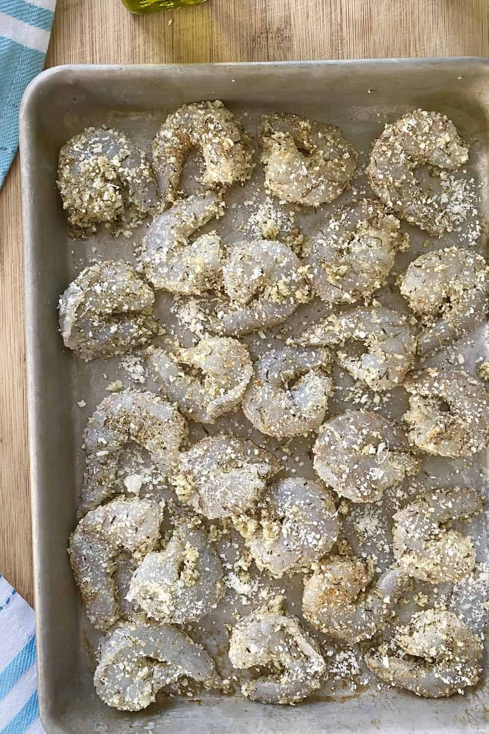 A baking sheet with raw seasoned shrimp and parmesan cheese.