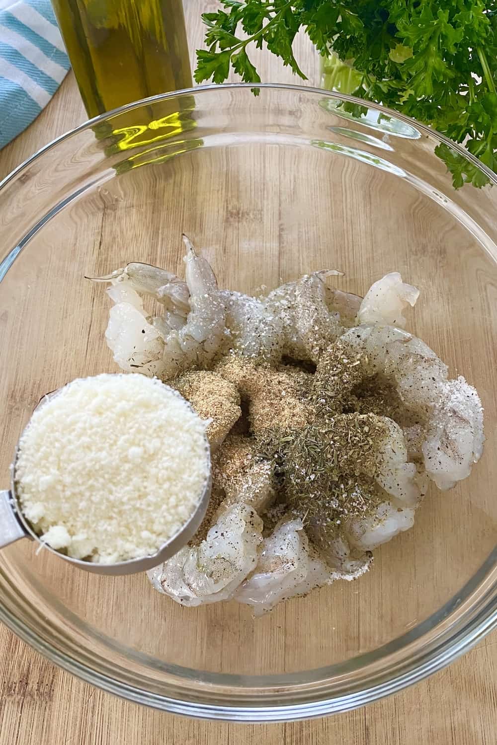 Raw shrimp in a bowl with seasonings and adding parmesan cheese.