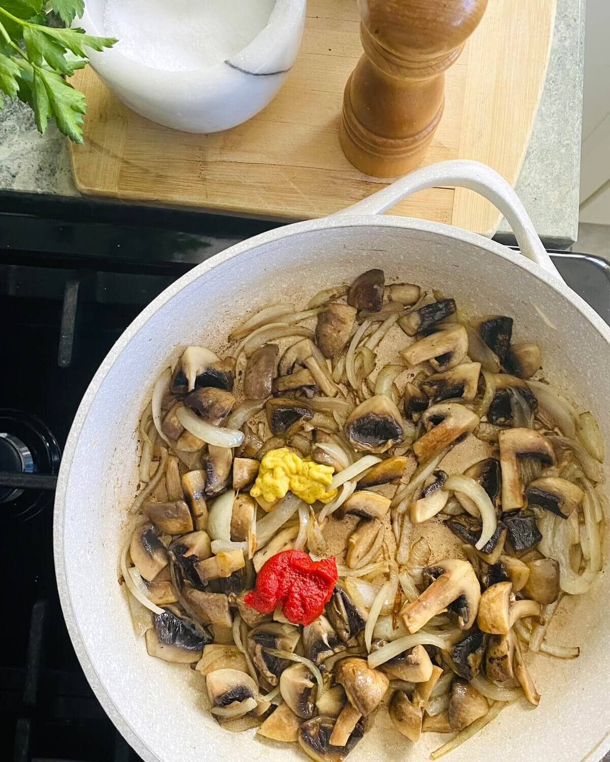 Adding tomato paste and mustard to sauteed mushrooms and onions.