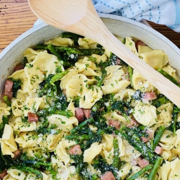 pan with a wodden spoon and tortellini pasta with ham and asparagus