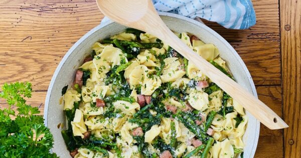 pan with a wodden spoon and tortellini pasta with ham and asparagus