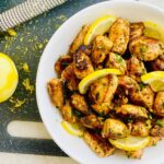 A bowl of lemon and herb chicken bites with lemon wedges.