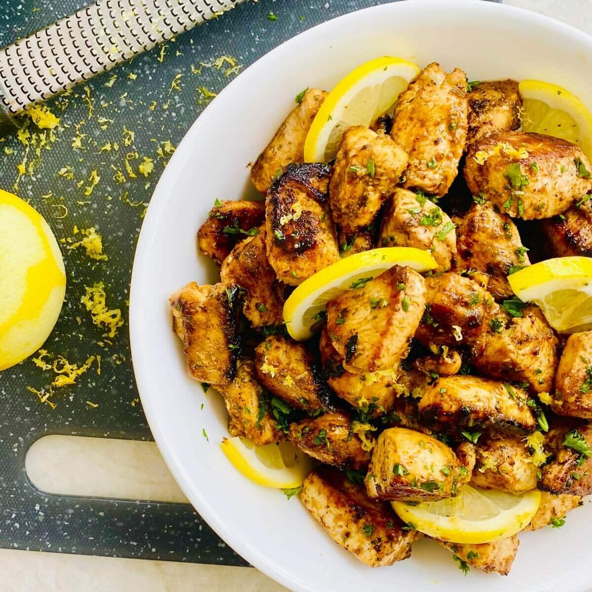 A bowl of lemon and herb chicken bites with lemon wedges.