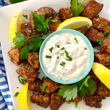 Blackened tuna bites on a plate with dipping sauce and lemons.