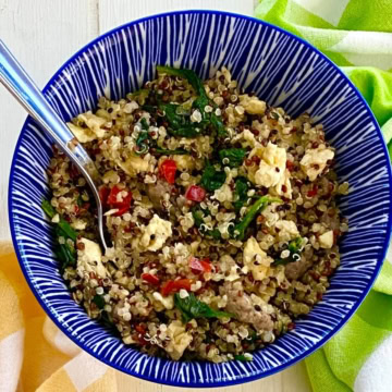 A quinoa breakfast bowl with scrambled eggs, sausage, and spinach.