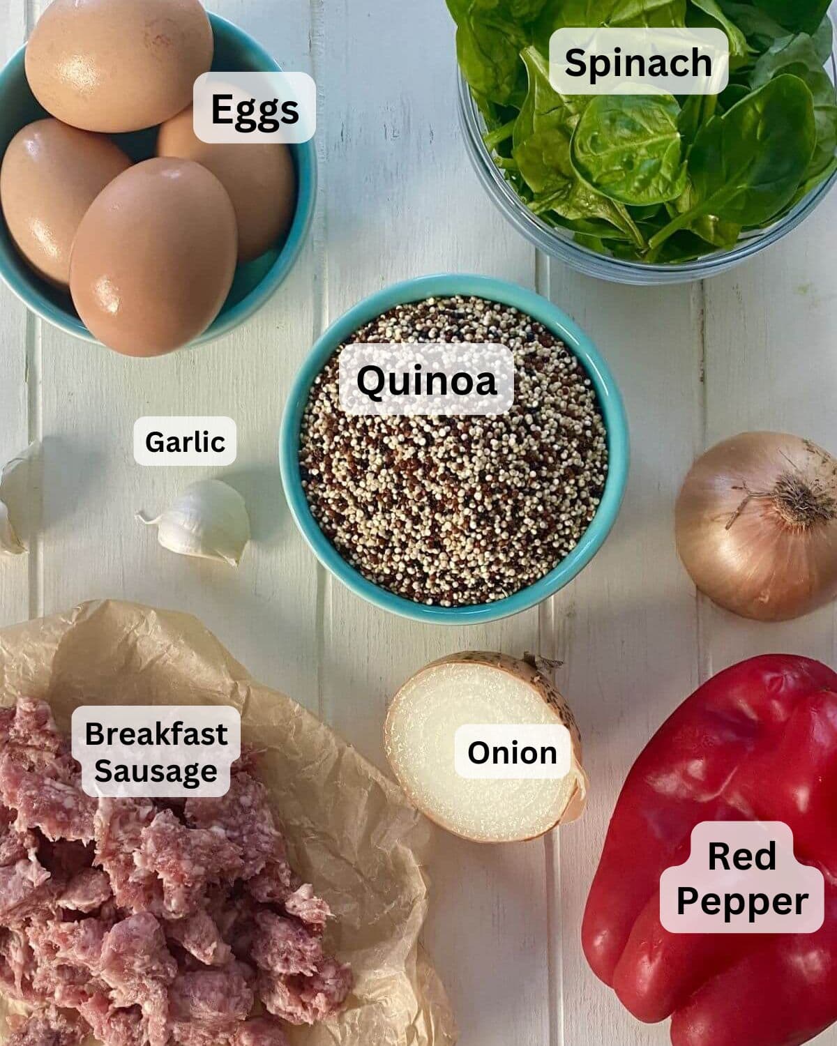 Eggs, quinoa, sausage, garlic, spinach, onion, and red pepper on a board.