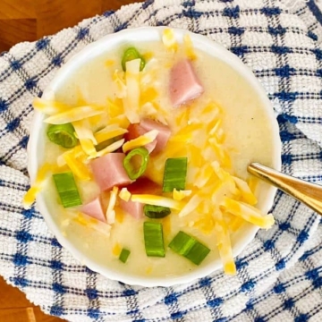 bowl of cheesy ham and potato soup with a blue and white check napkin.