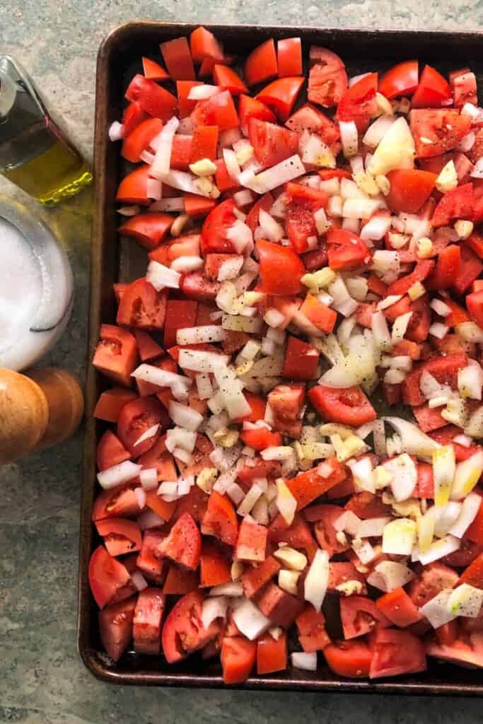 Chopped tomatoes, onions and garlic on a baking sheet.