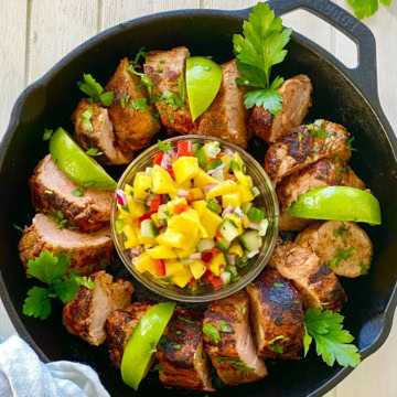 A cast iron skillet with pork tenderloin and mango salsa.