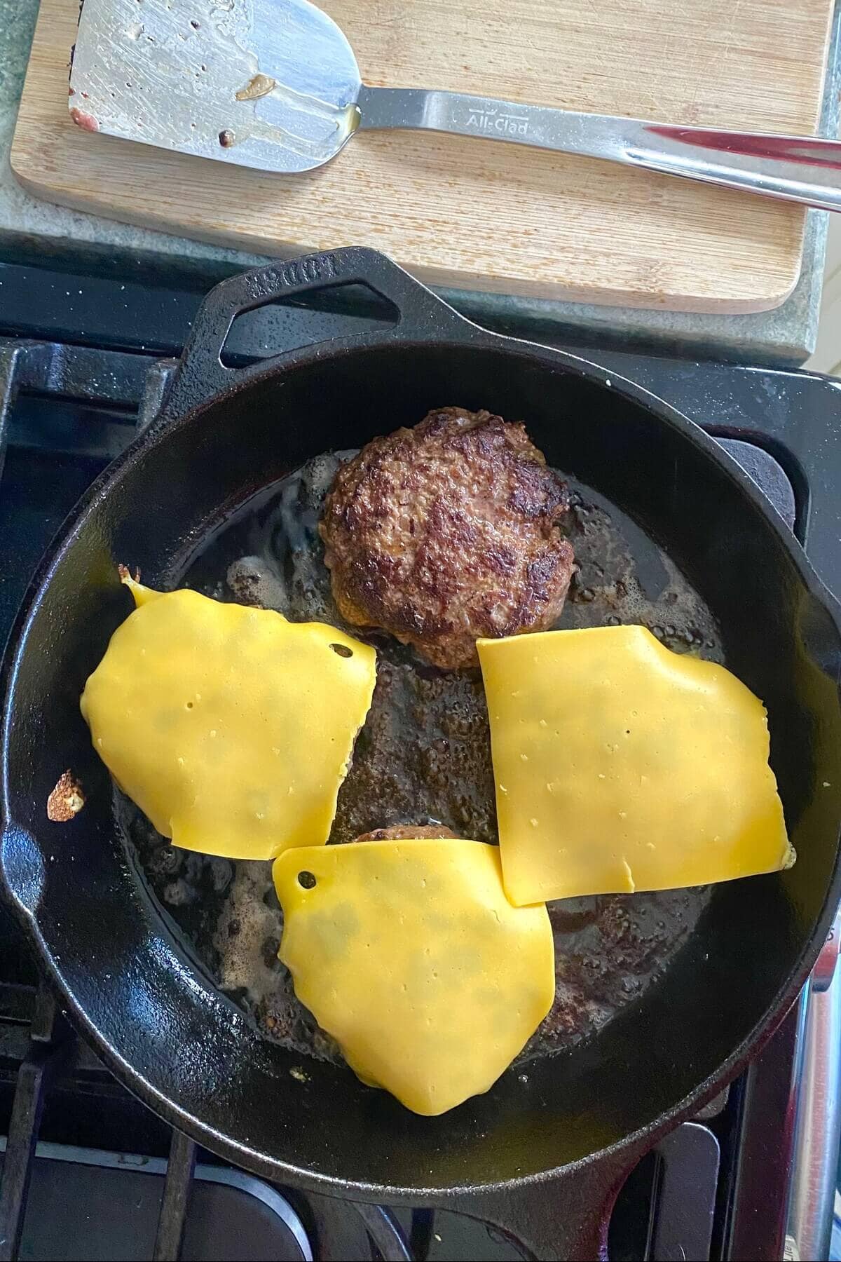 Four hamburgers cooking in a cast iron skillet.