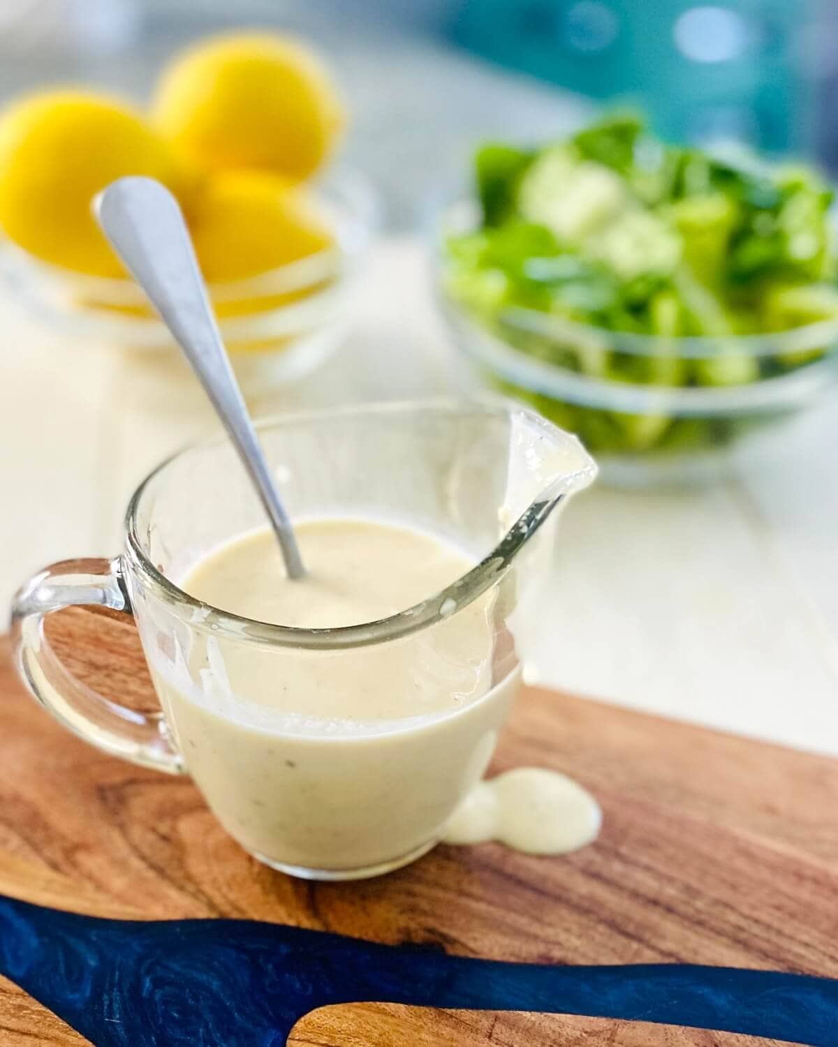 A glass pitcher of dressing, bowl of lemons and a bowl of lettuce.