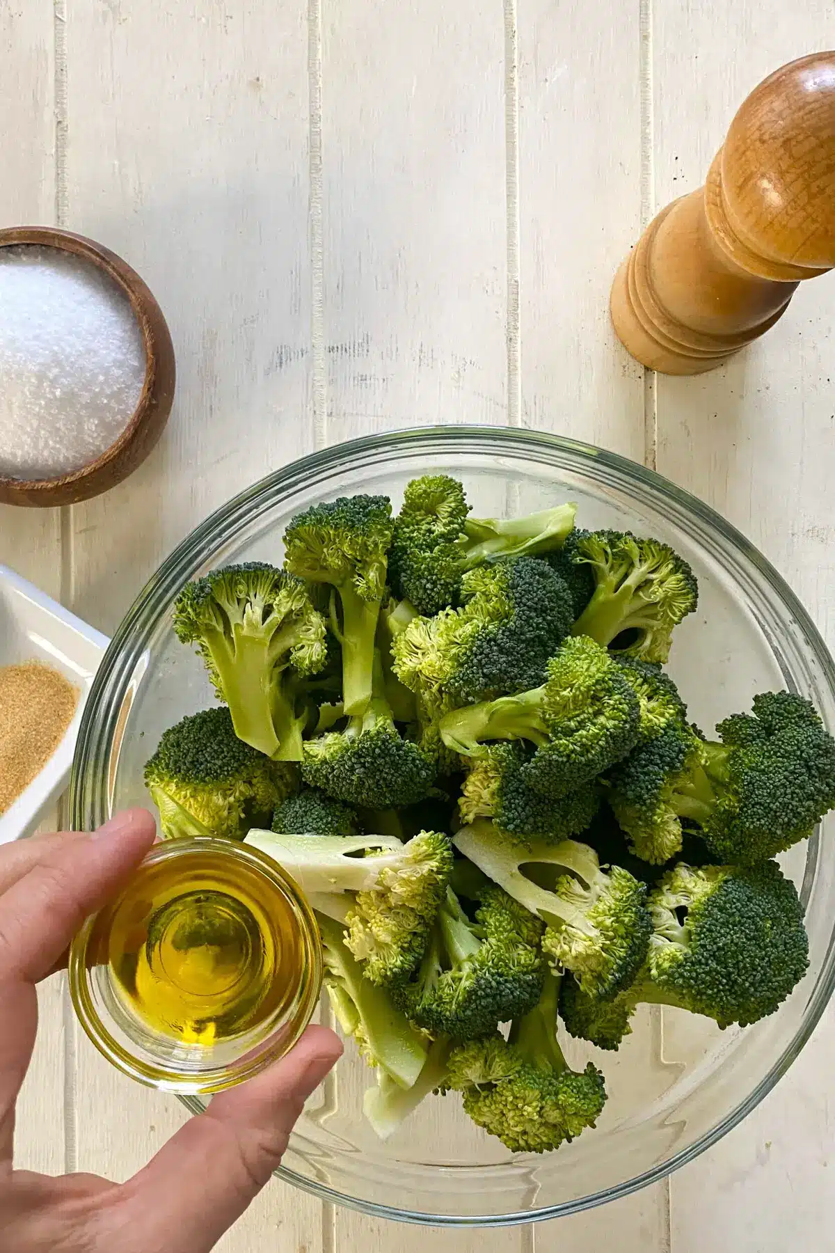 raw broccoli florets in a glass bowl and adding olive oil.