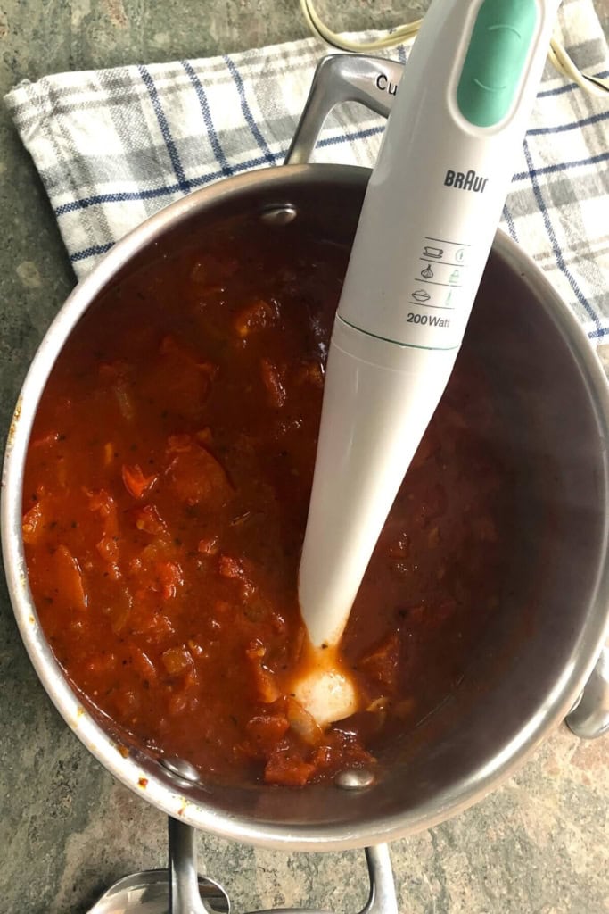 Immersion blender and tomato bisque with basil in a pot.