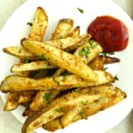 A plate of oven baked french fires with ketchup.