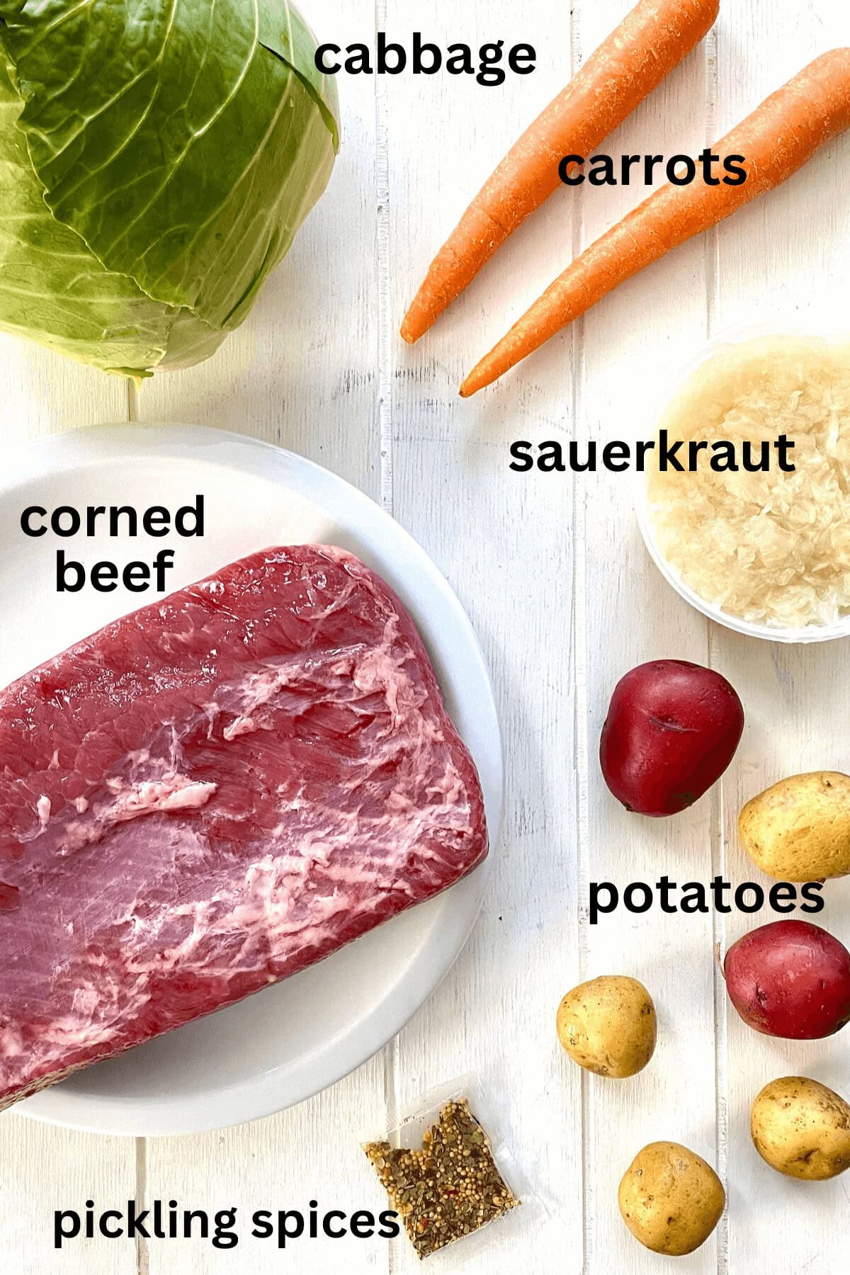 Cabbage, corned beef, sauerkraut, carrots, potatoes on a board.