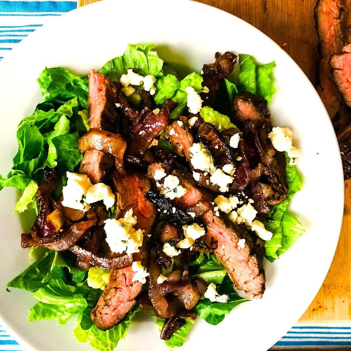 A serving of steak salad with roasted onions and blue cheese.