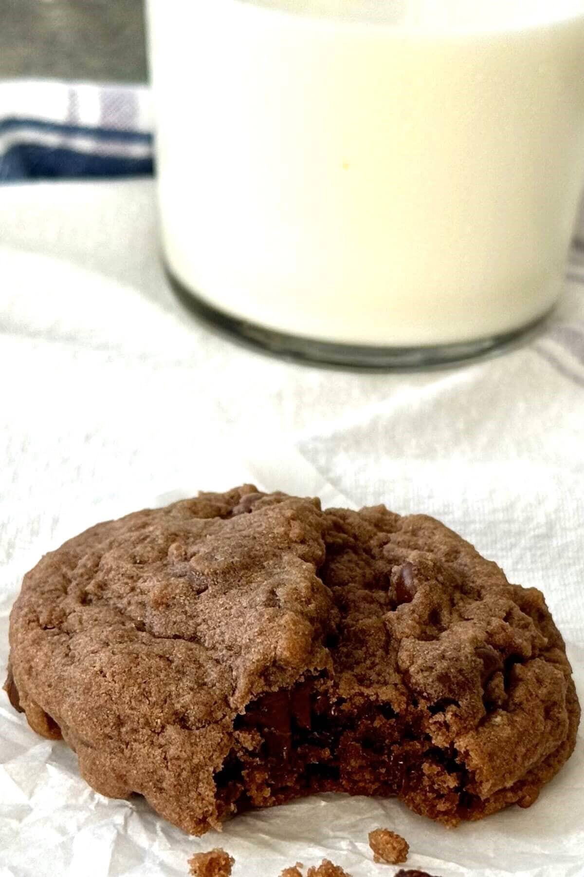 A chocolate cookie with a bite out and a glass of milk.