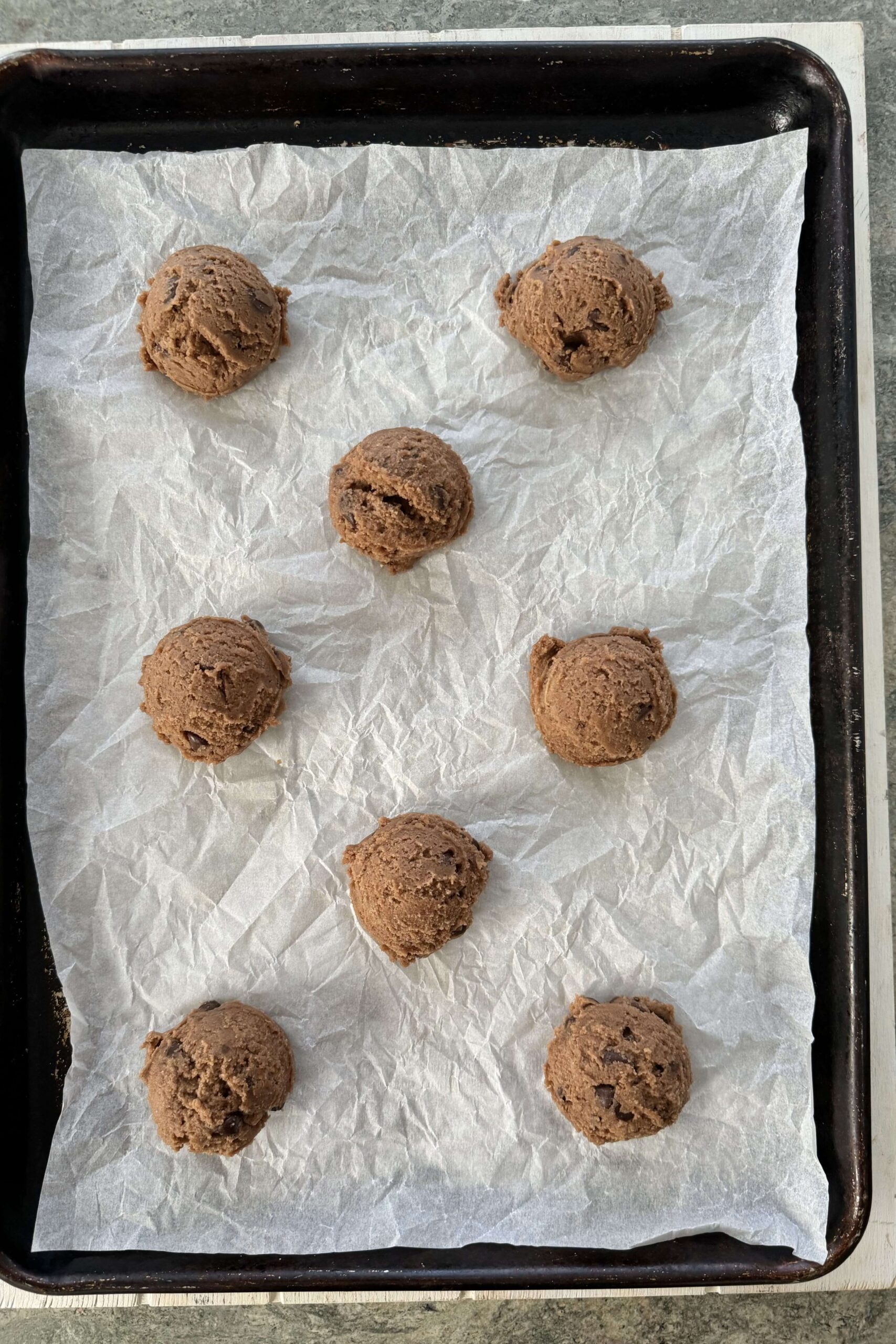 Cookie dough balls on a parchment paper line baking sheet.