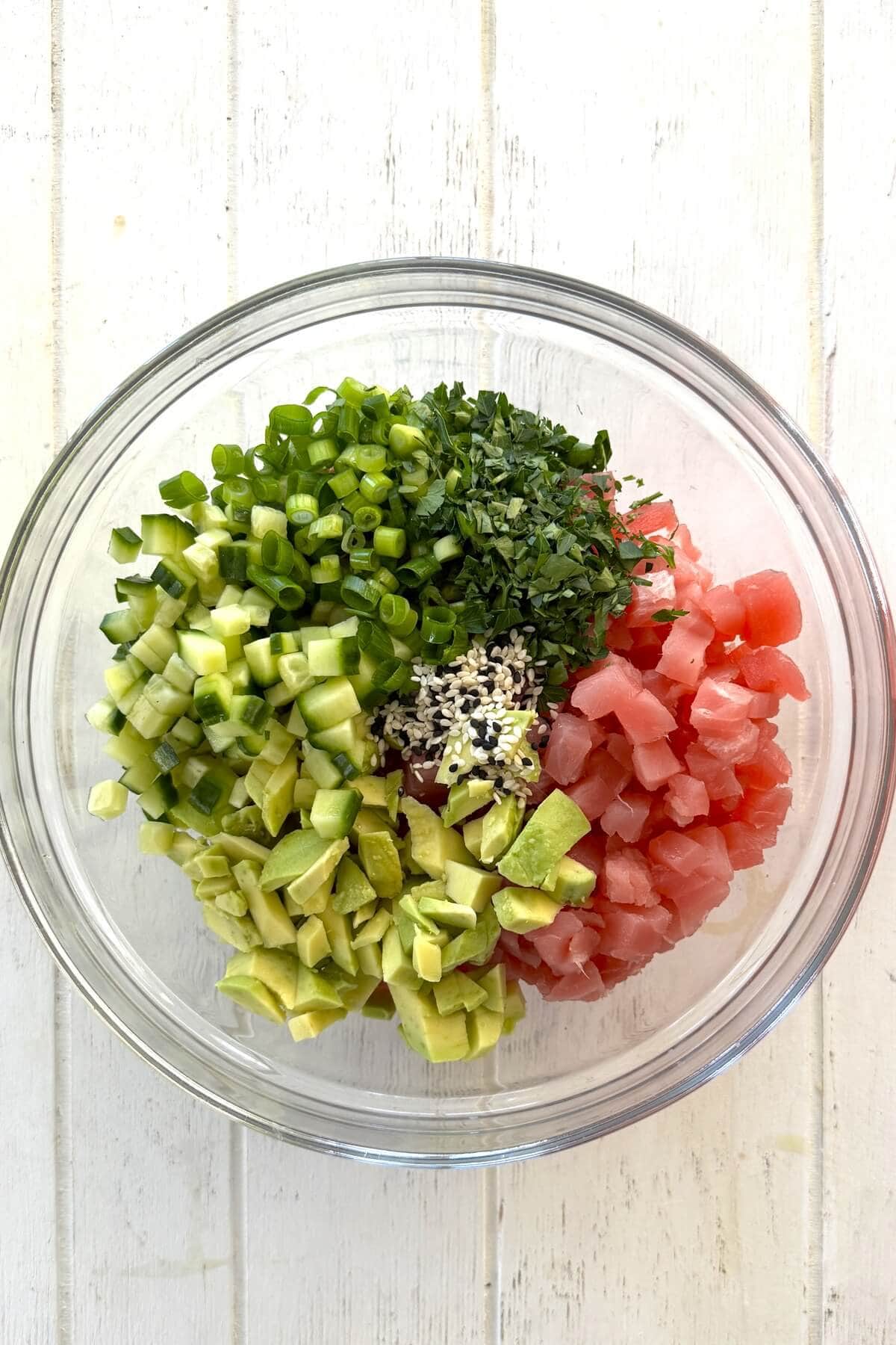 A bowl with diced tuna, avocado, cucumber, and green onions.