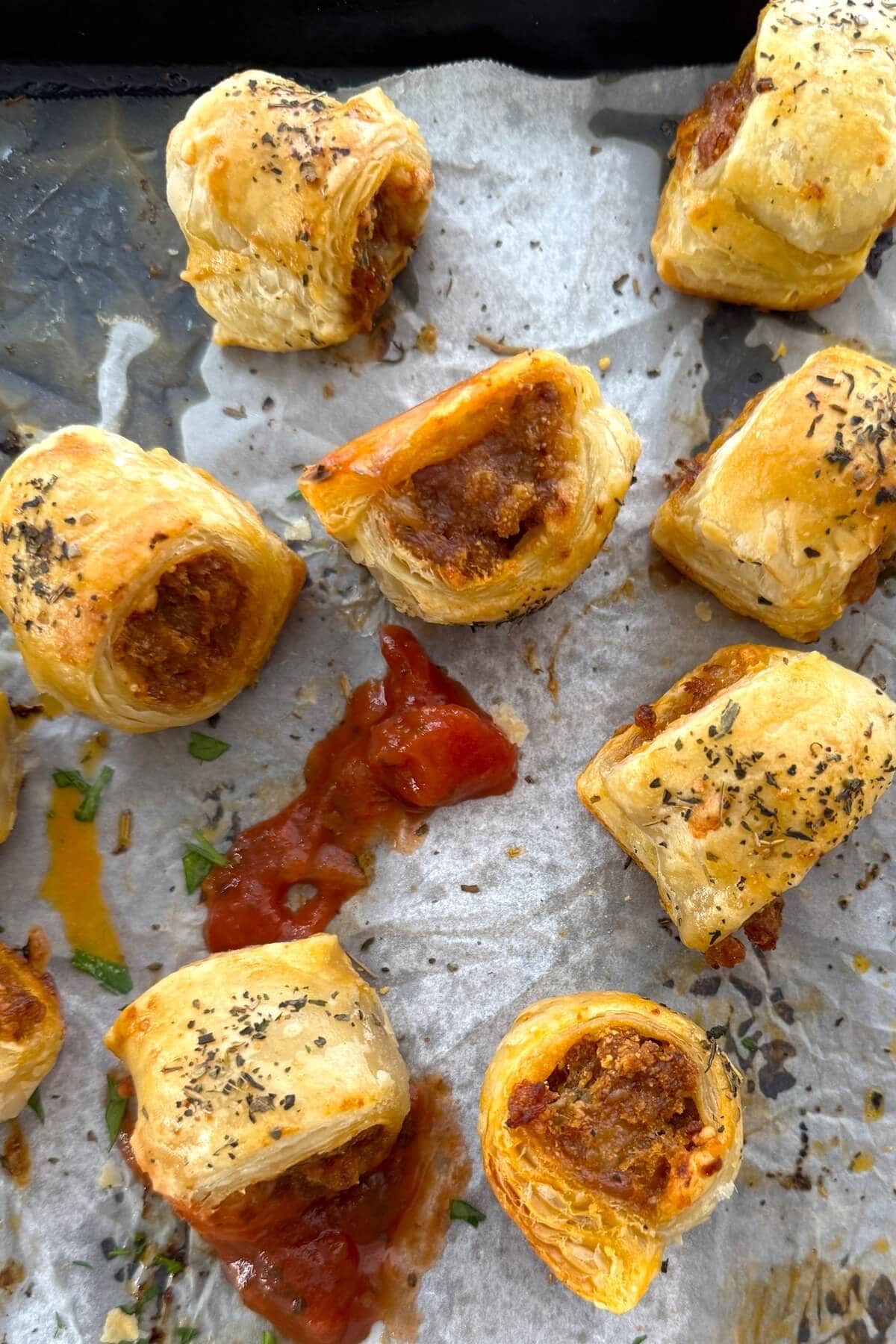 Sausage rolls on a baking sheet with marinara sauce.