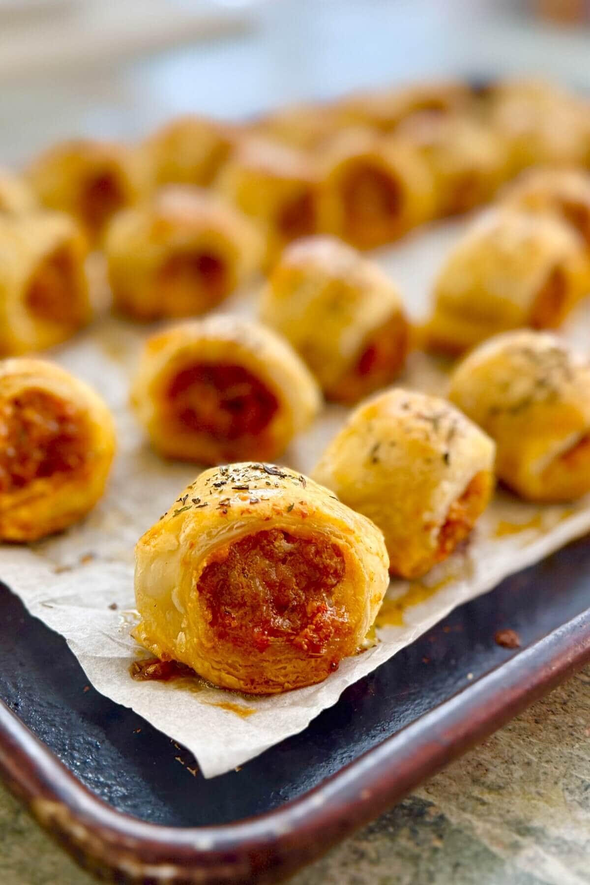 Puff pastry rolls with Italian sausage on a baking sheet.