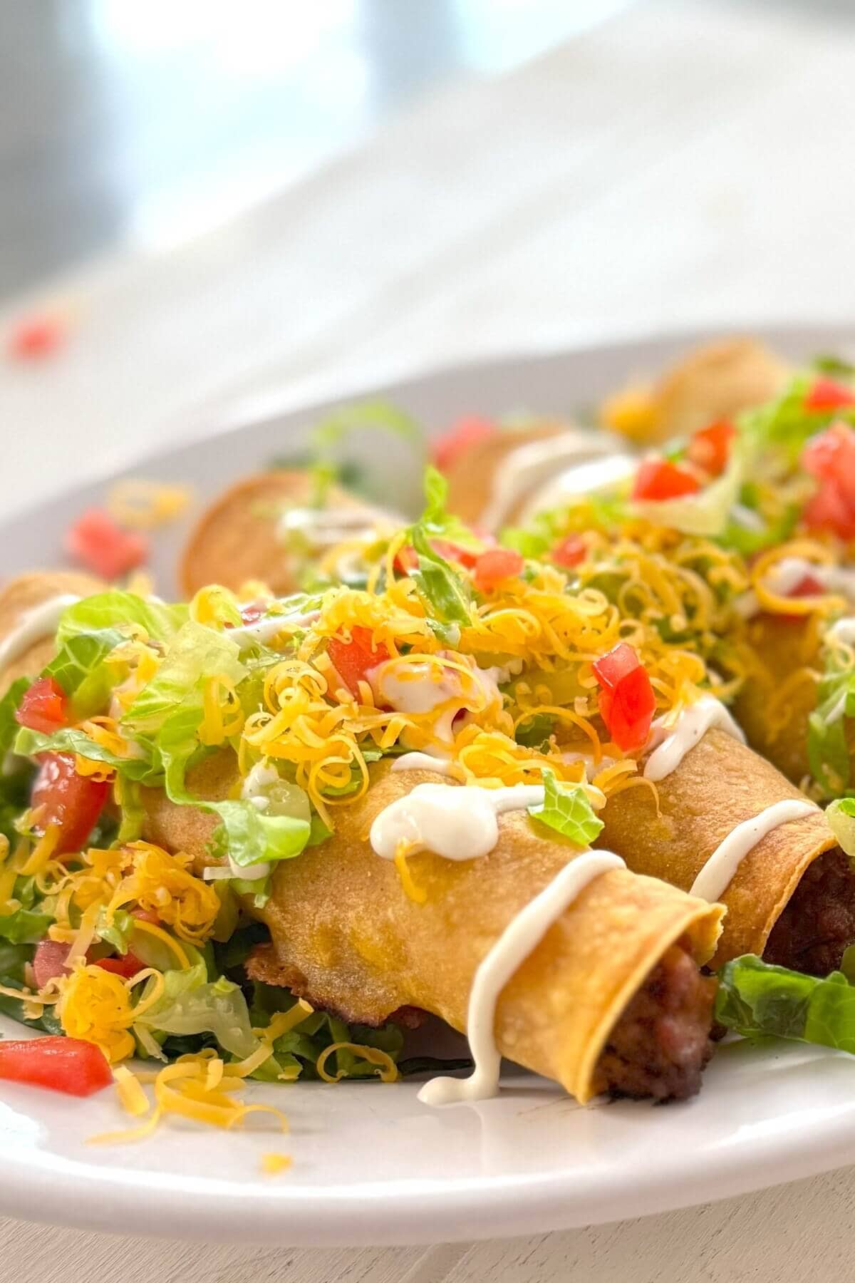 Rolled tacos with sour cream, cheese, lettuce and tomatoes.