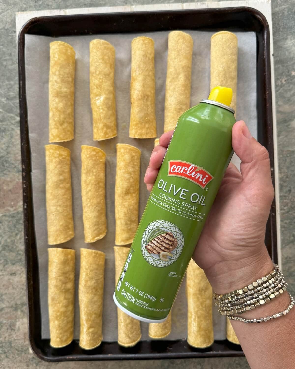 Rolled tacos on a baking sheet and a can of cooking spray.